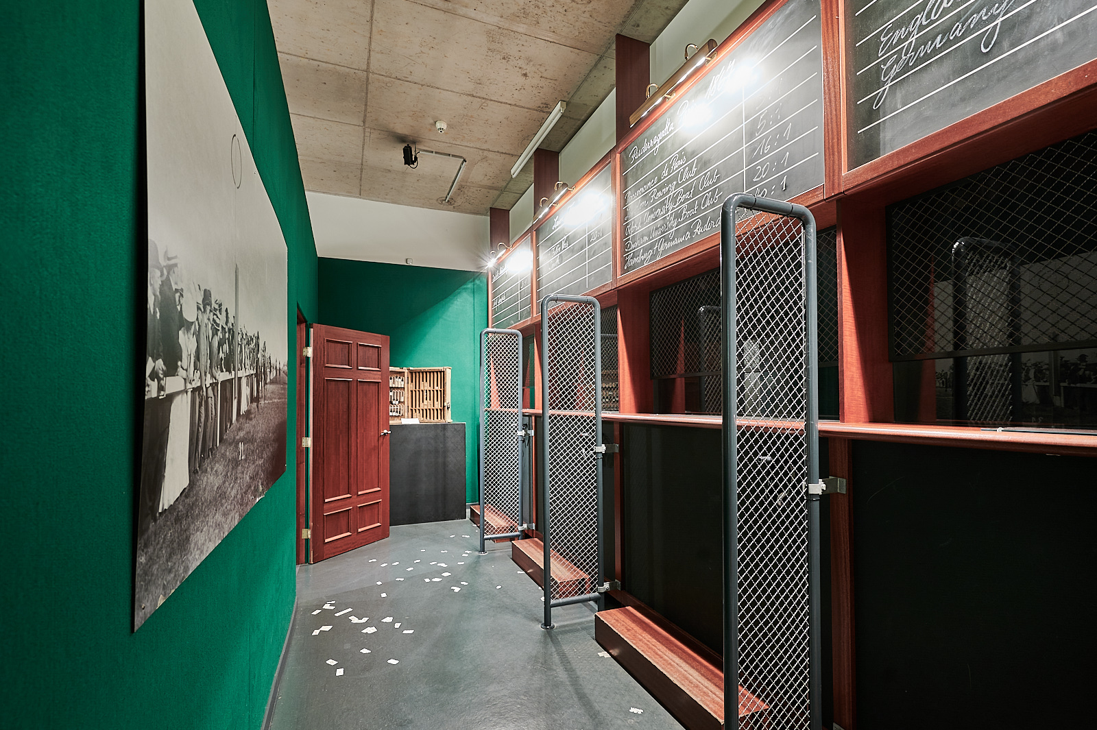 Das Foto wurde in einem alten Wettbüro gemacht. Es ist ein kleiner Raum mit drei Kabinen. Der Raum stellt ein Wettbüro von früher dar. Auf dem Boden sind alte Wettscheine dargestellt. Der Raum ist grün.