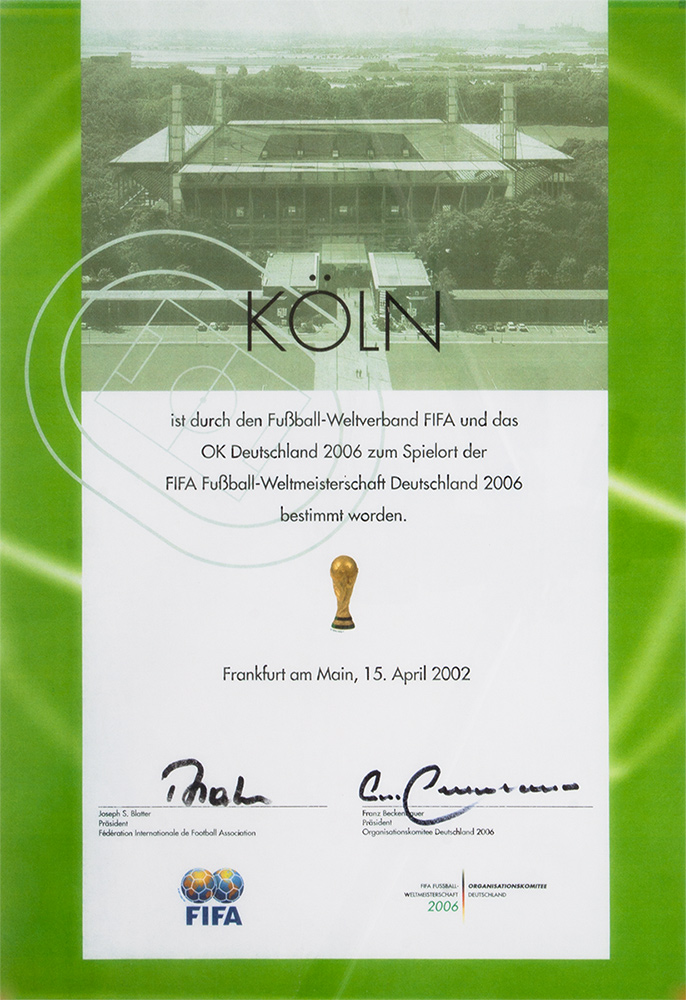 Ernennungsurkunde zum Spielort der Fußballweltmeitserschaft mit Fotografie des Rheinenergiestadions