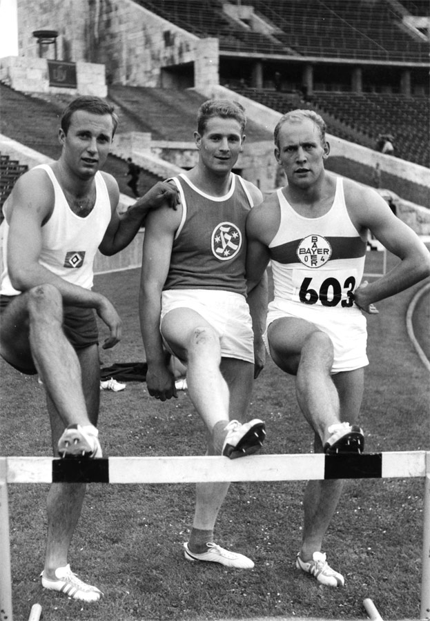 Fotografie in Schwarz und Weiß von Manfred Bock, Werner von Moltke und Willi Holdorf mit jeweils einem Fuß auf einer Hürde