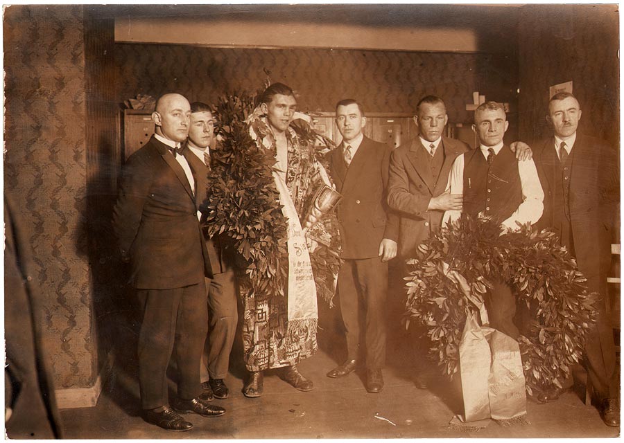 Fotografie von Max Schmeling mit Kranz umgeben von mehreren Männern in Anzug