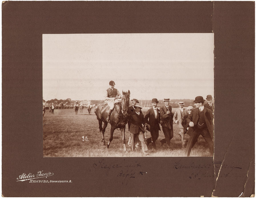 Reiter auf Pferd in Begleitung mehrerer Männer in Anzug und Hut