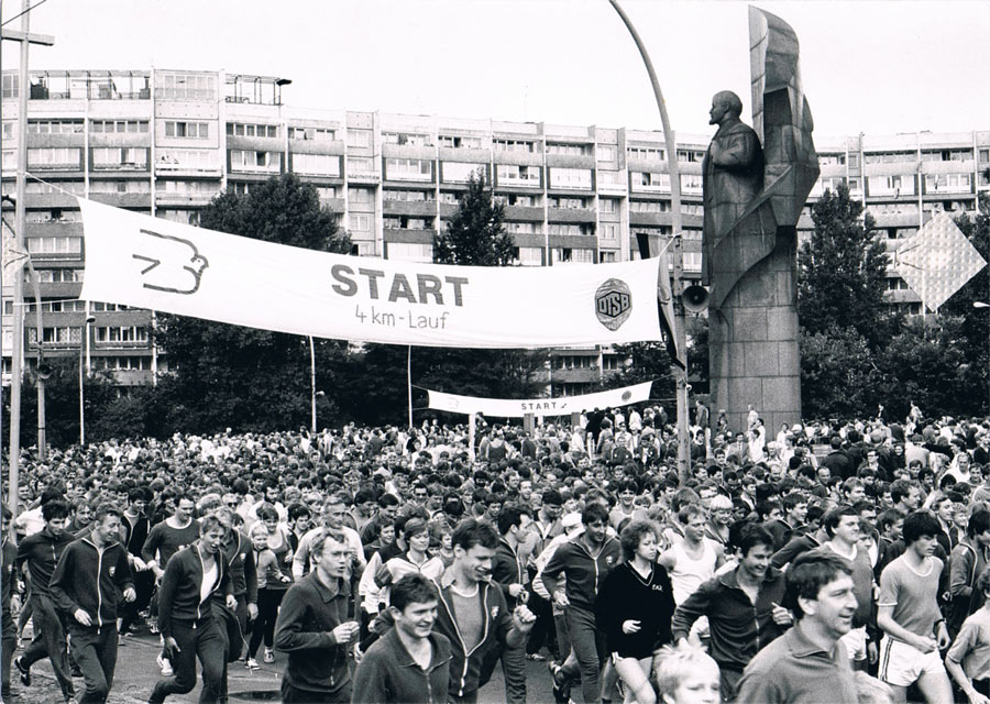 Fotografie zahlreicher Sportler und Sportlerinnen beim Start zum 3. Friedenslauf. Im Hintergrund eine Statue Lenins