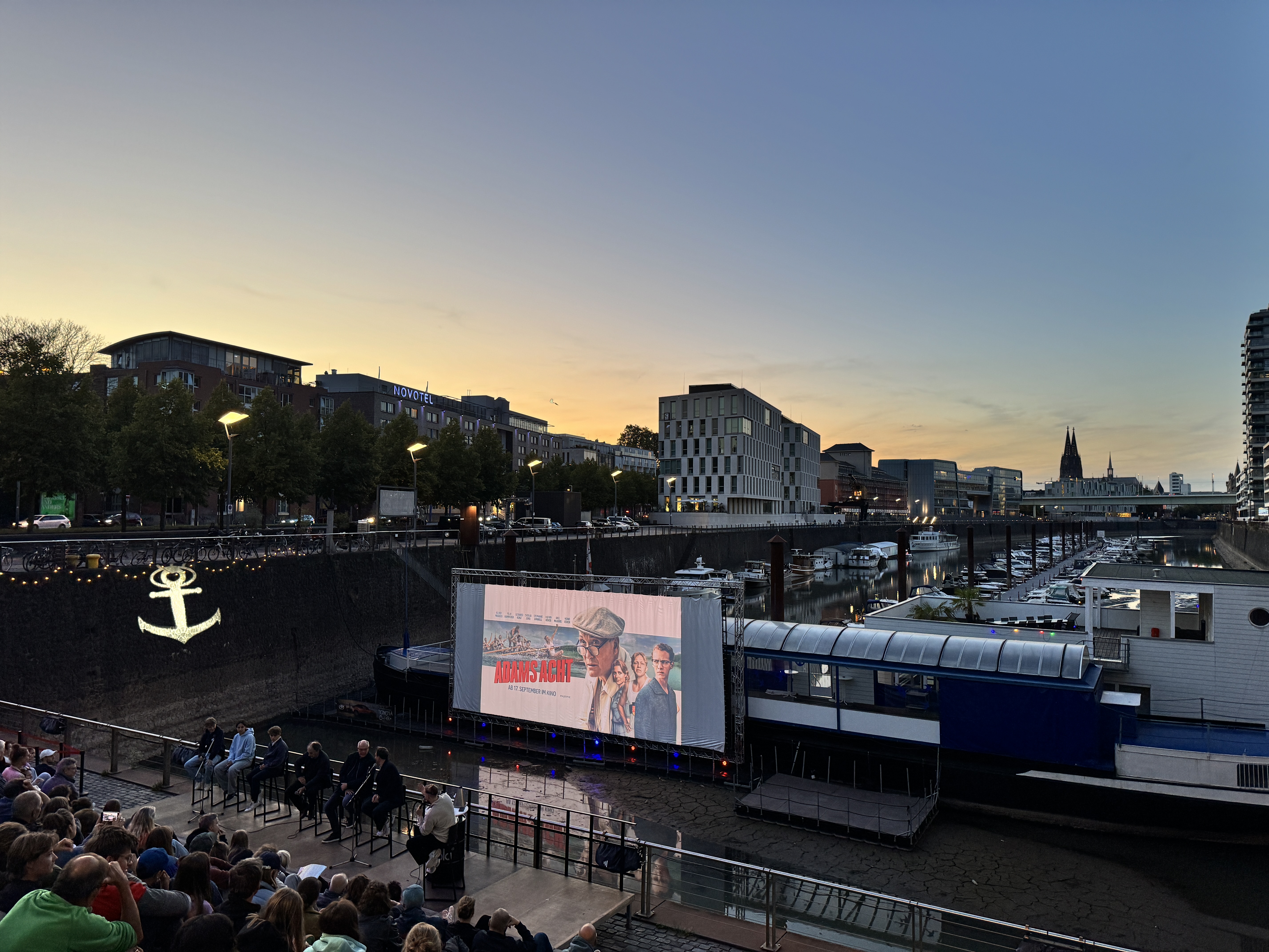 Das Bild zeigt die abendliche Stimmung während der Filmvorführung, Im Bildvordergrund sieht man die Vielzahl der Zuschauenden.