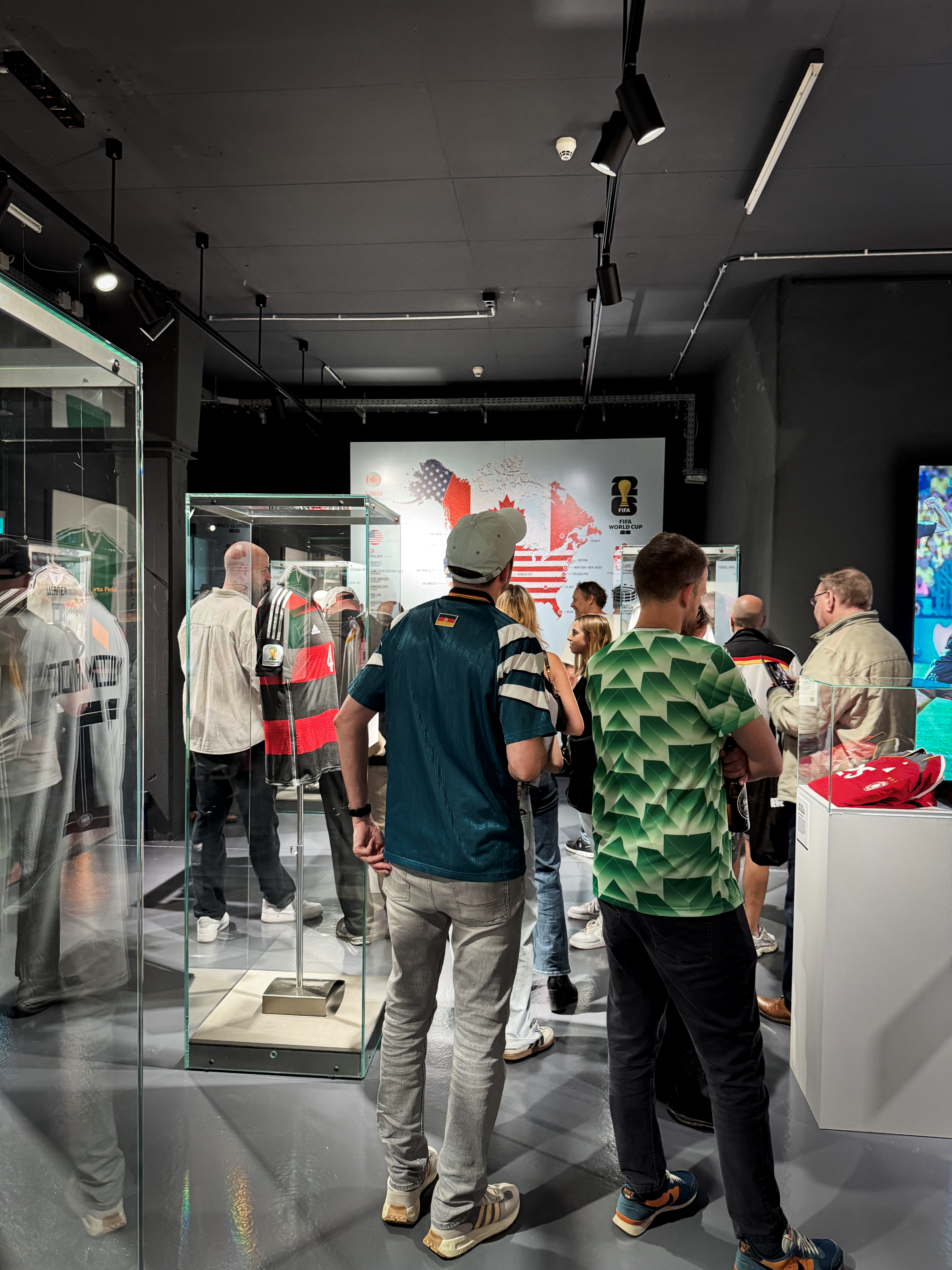 Einige Besuchende in Trikots betrachten die Ausstellung.