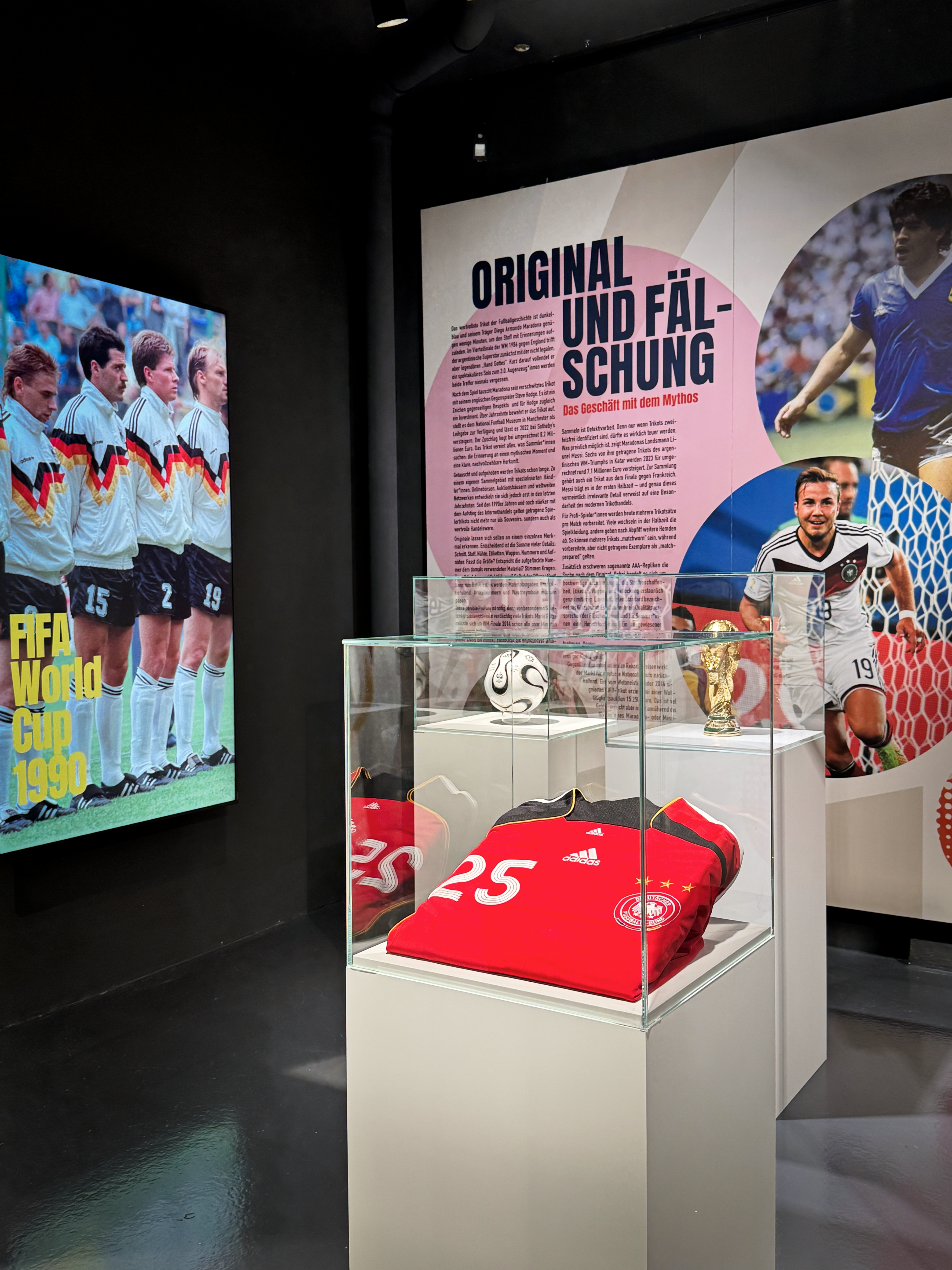 Ausschnitt der Ausstellung. Links ein Screen mit dem Foto der Nationalelf bei der WM 1990. Rechts ein Ball und ein rotes Trikot.