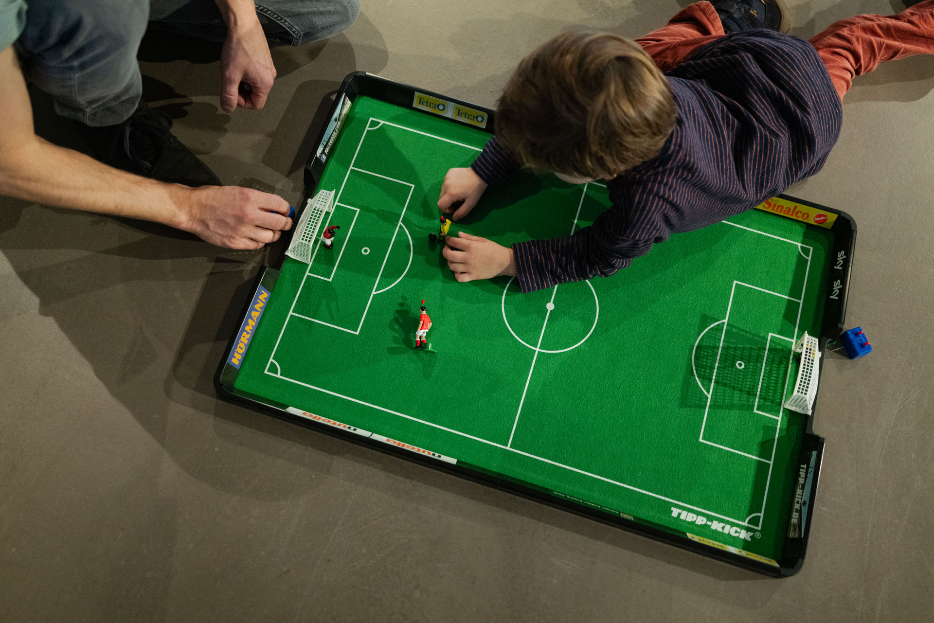 Es ist ein Tipp-Kick-Feld von oben zu sehen. Ein Vater und sein Sohn spielen.