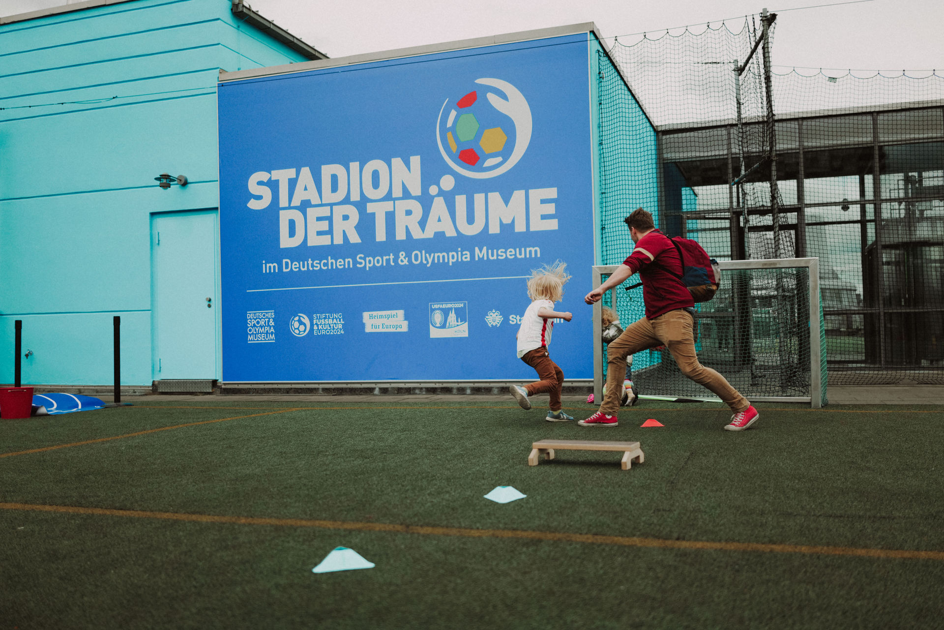 Es wird auf dem Dach gespielt. Eine erwachsene Person steht im Tor, Kinder versuchen den Ball reinzutreffen.