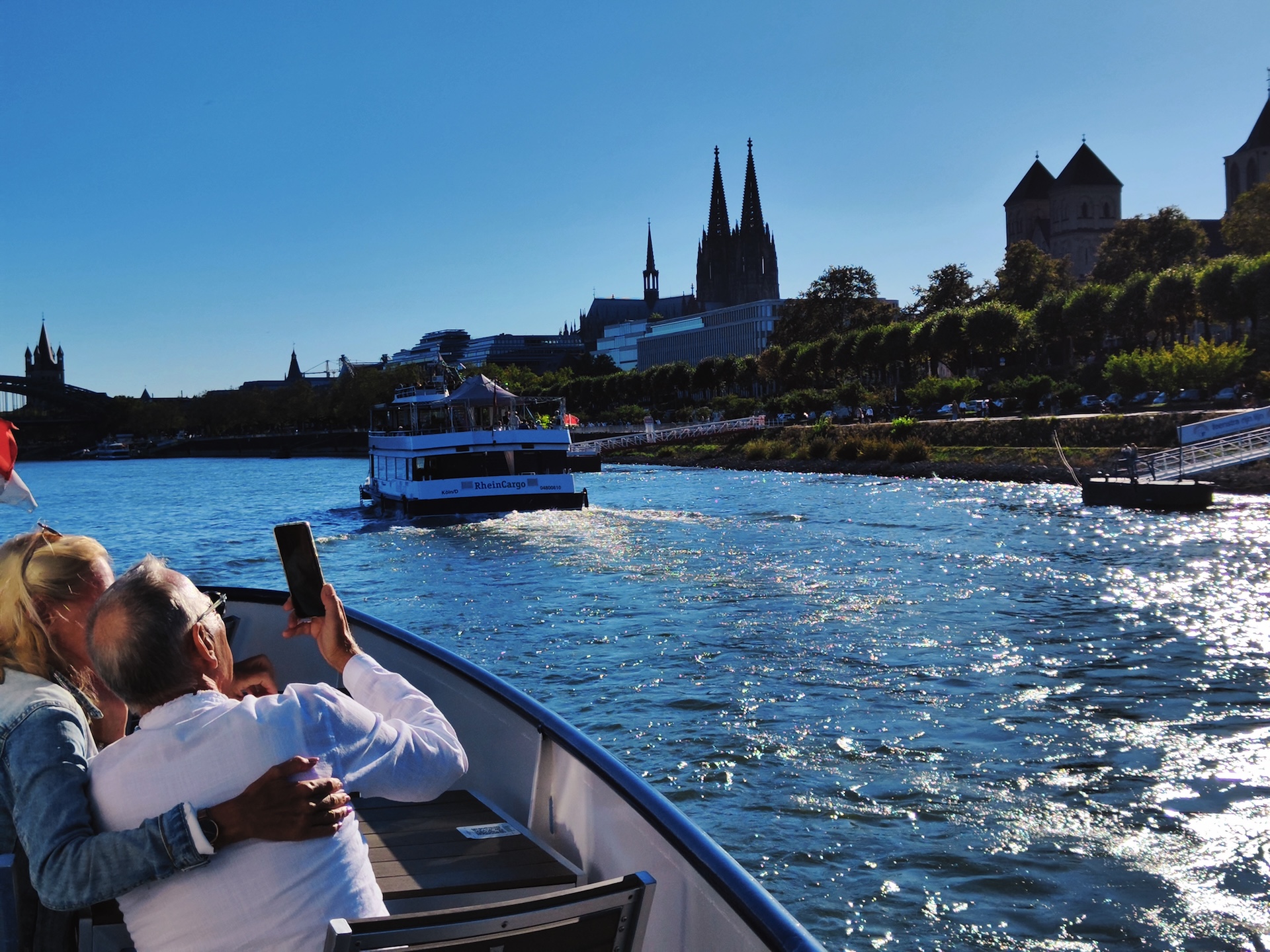 Auf dem Bild sind zwei Personen in einem Boot zu sehen. Das Boot ist auf dem Rhein unterwegs. Im Hintergrund ist der Dom sichtbar.