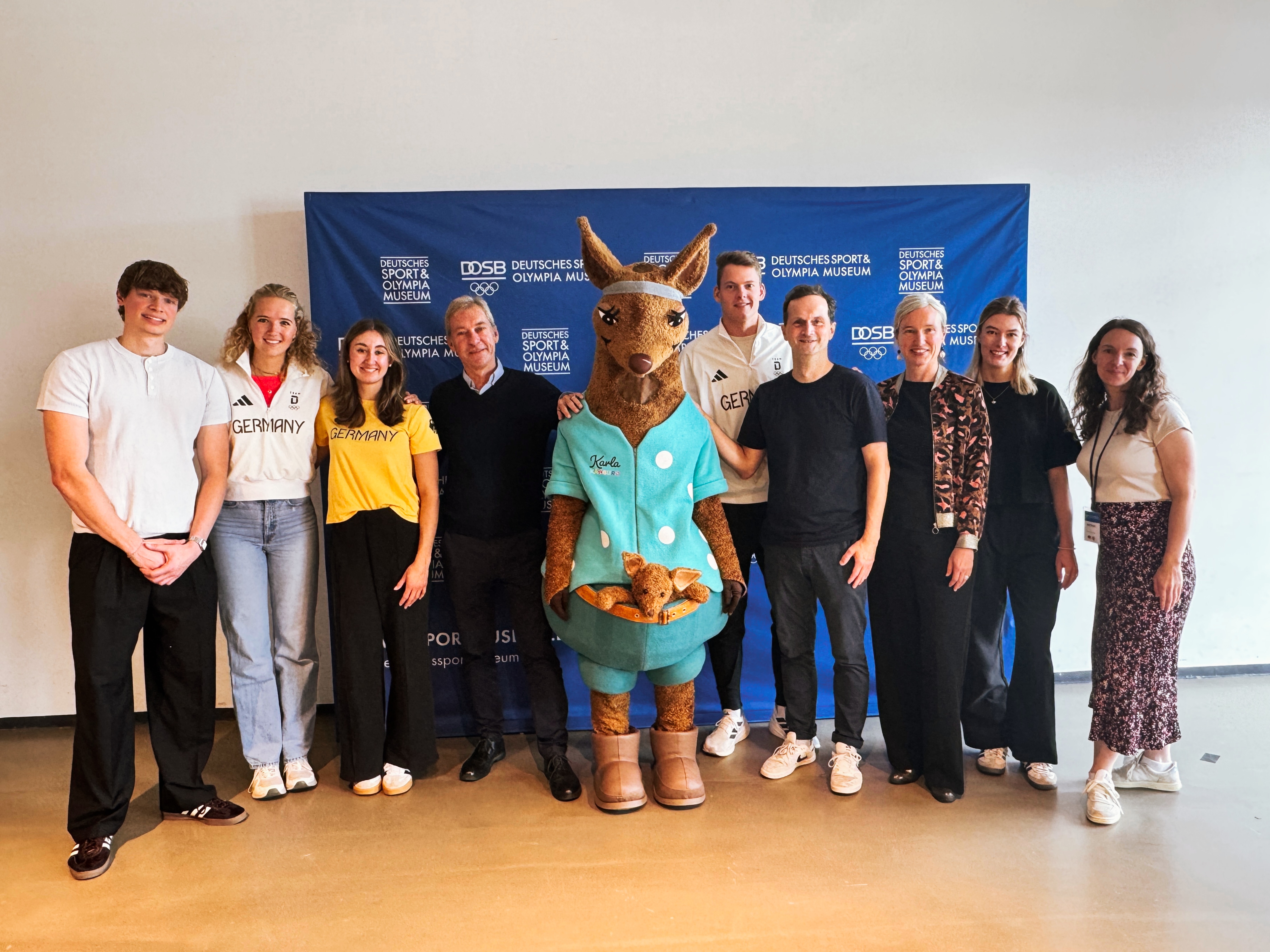 Mehrere Personen und das Maskottchen Karla Känguru stehen vor einer Pressewand des Museums.