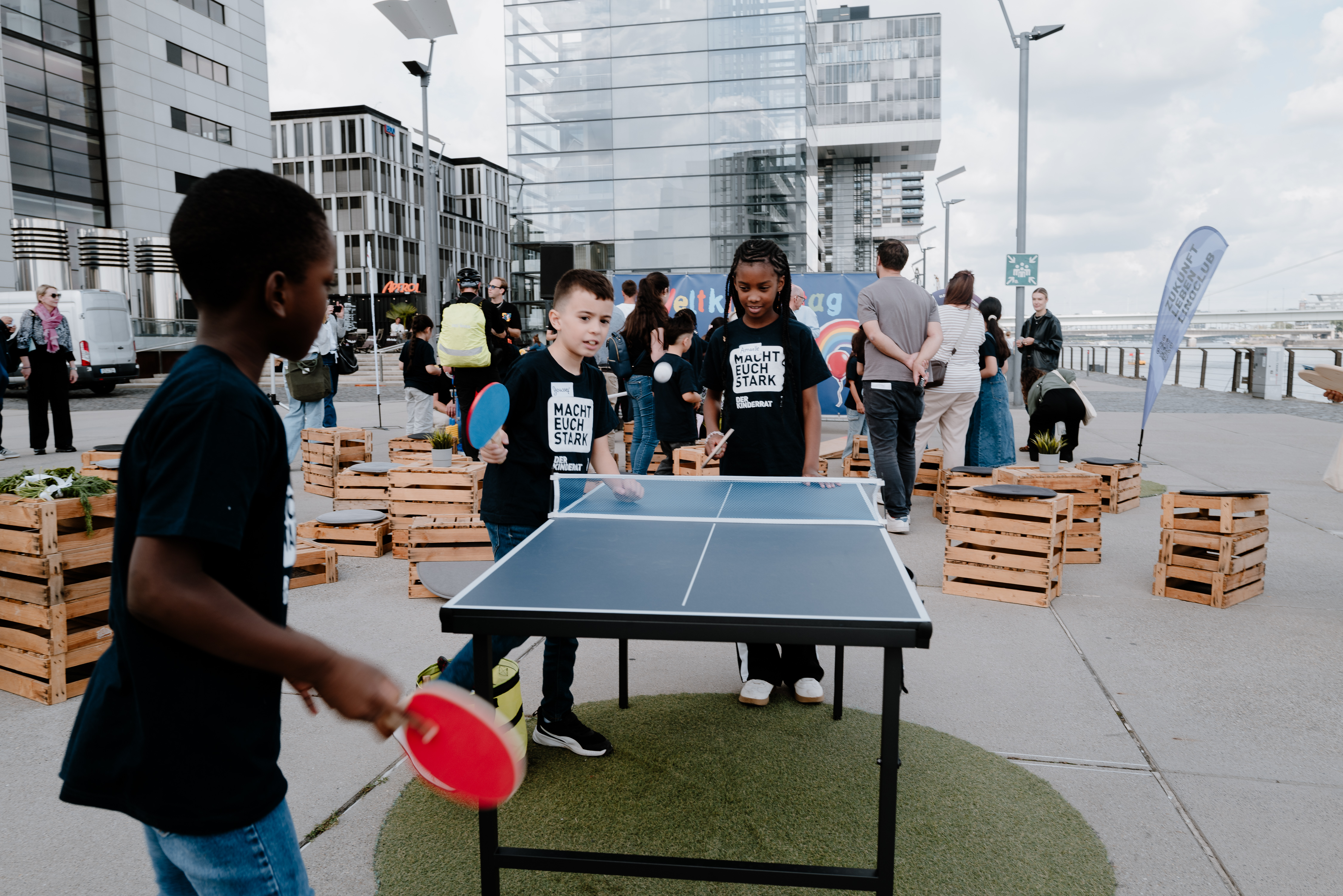 Es sind Kinder beim Tischtennisspielen zu sehen. Im Hintergrund sind weitere Spiel-Stationen im Rheinauhafen aufgebaut.