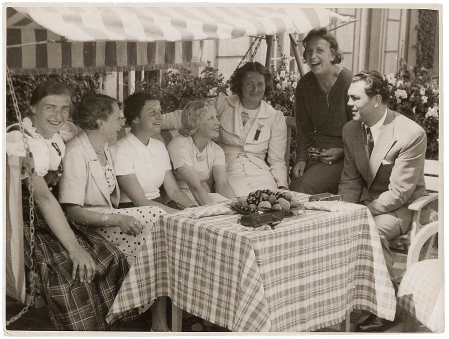 Max Schmeling am Tisch sitzend daneben auf Hollywoodschaukel mehrere deutsche Sportlerinnen