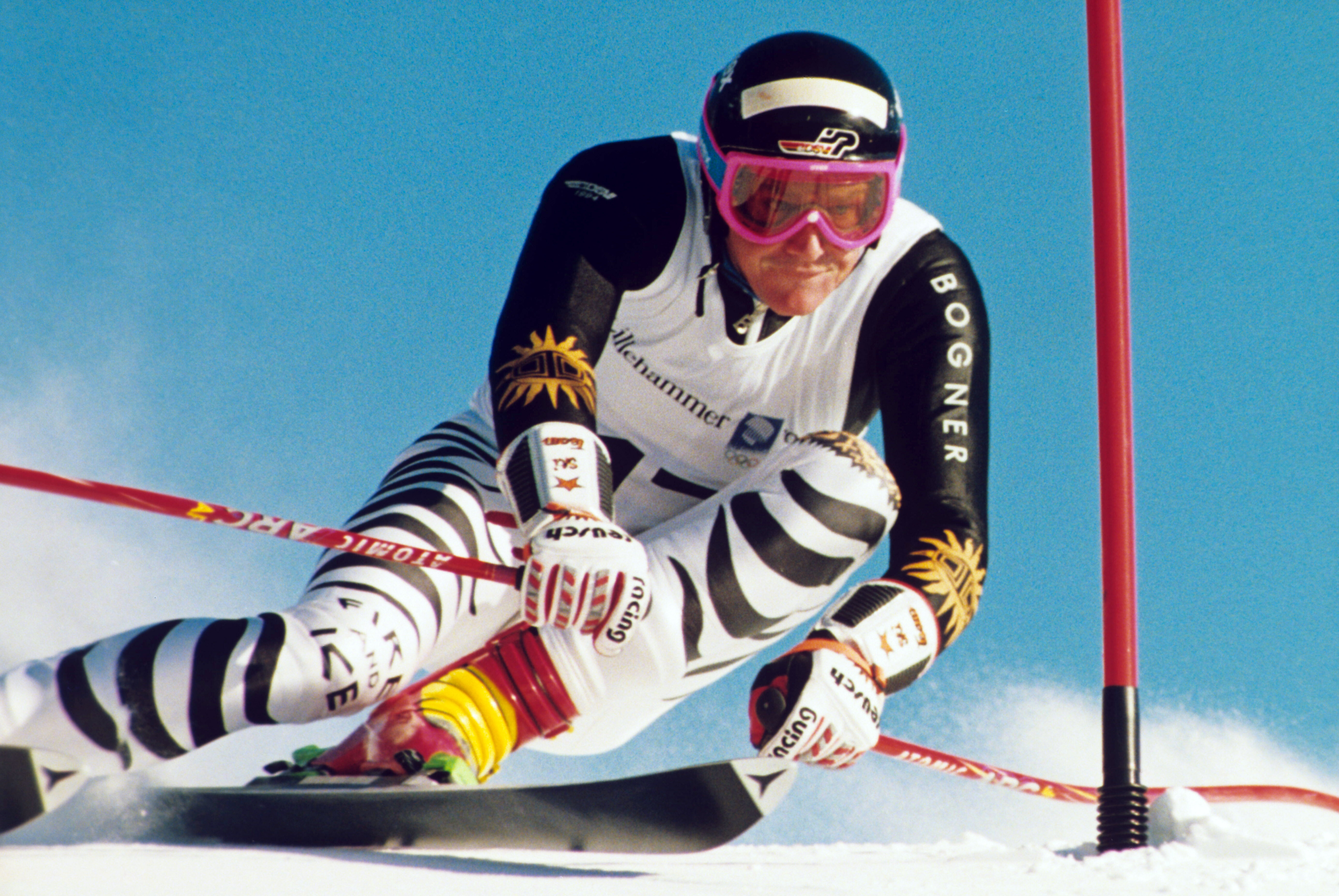 Auf dem Foto ist ein Skifahrer zu sehen, der gerade fährt. Der Skifahrer hat einen schwarz-weißen Skianzug an und einen schwarzen Helm. Auf seinem Helm steht DSV. Er fährt an einer roten Stange vorbei.